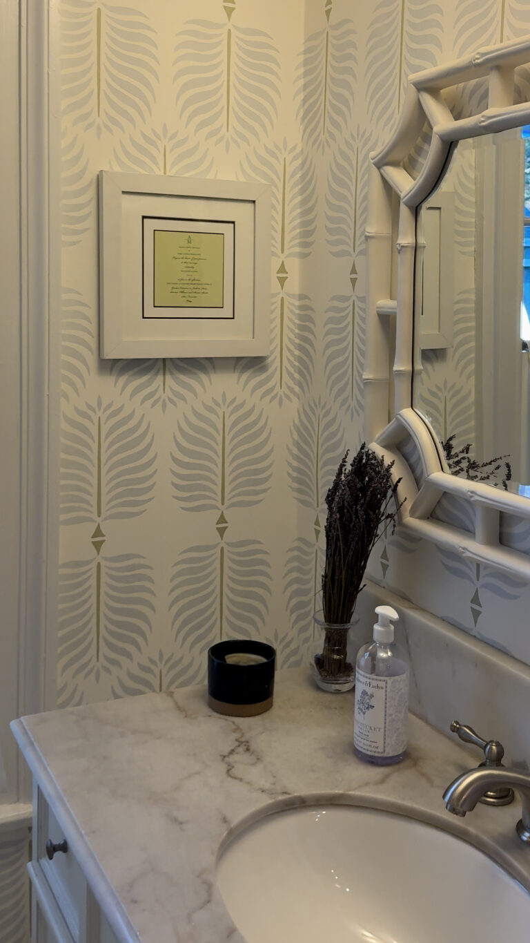 Bathroom countertop with a sink, soap bottle, candle holder, dried lavender, and patterned wallpaper.