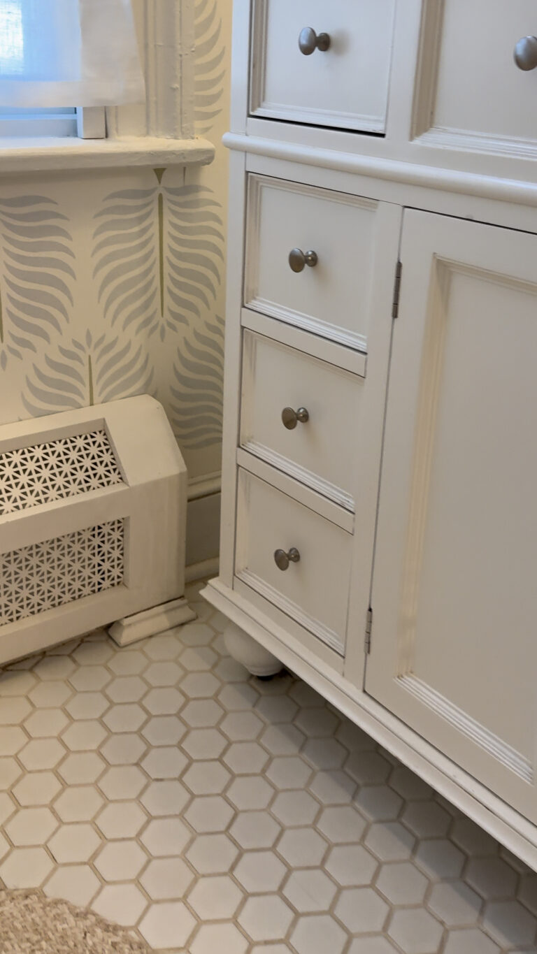 Bathroom remodeling by Omega Development in Connecticut. Corner of a bathroom with a white cabinet, decorative radiator cover, patterned wallpaper, and hexagon tile floor.