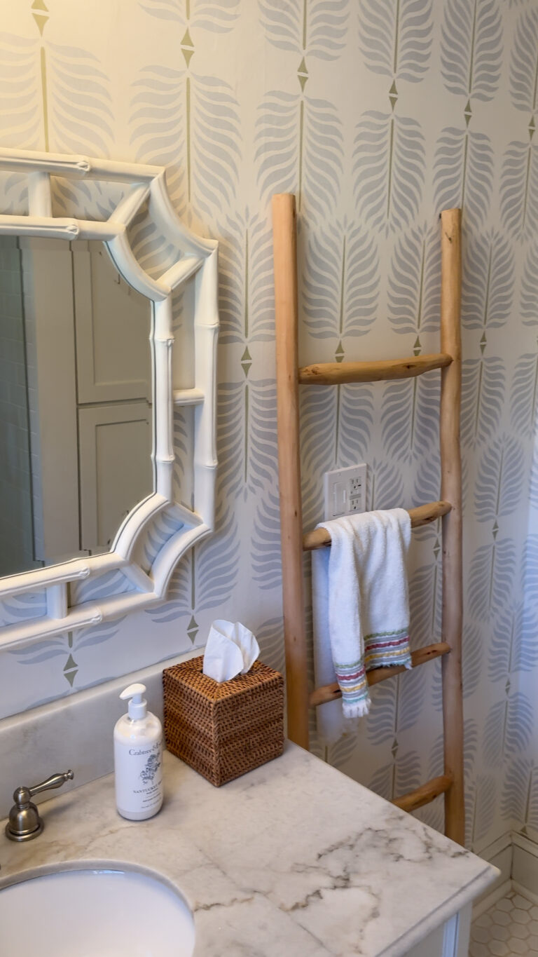 Bathroom wall with a decorative ceiling light, framed mirror, towel ladder, and patterned wallpaper.