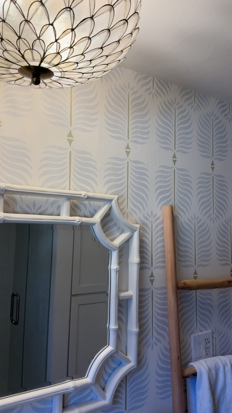 Bathroom wall with a decorative ceiling light, framed mirror, towel ladder, and patterned wallpaper.