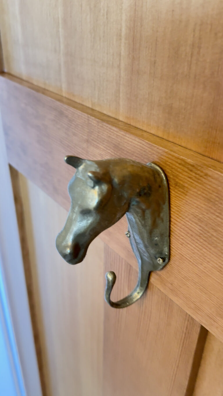 Decorative metal wall hook shaped like a horse’s head mounted on a wooden surface.