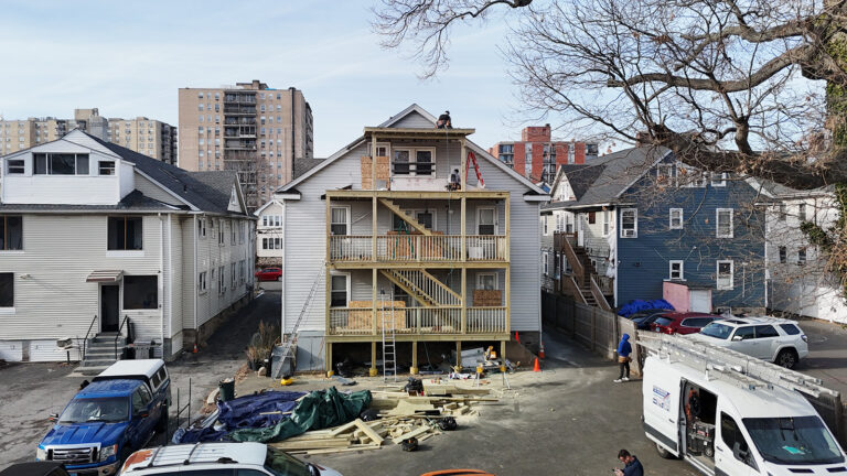 Deck installation contrcator in CT. Multi‑level wooden deck under construction, with railings, a central staircase, and plywood enclosing the lower section on the back of a house.