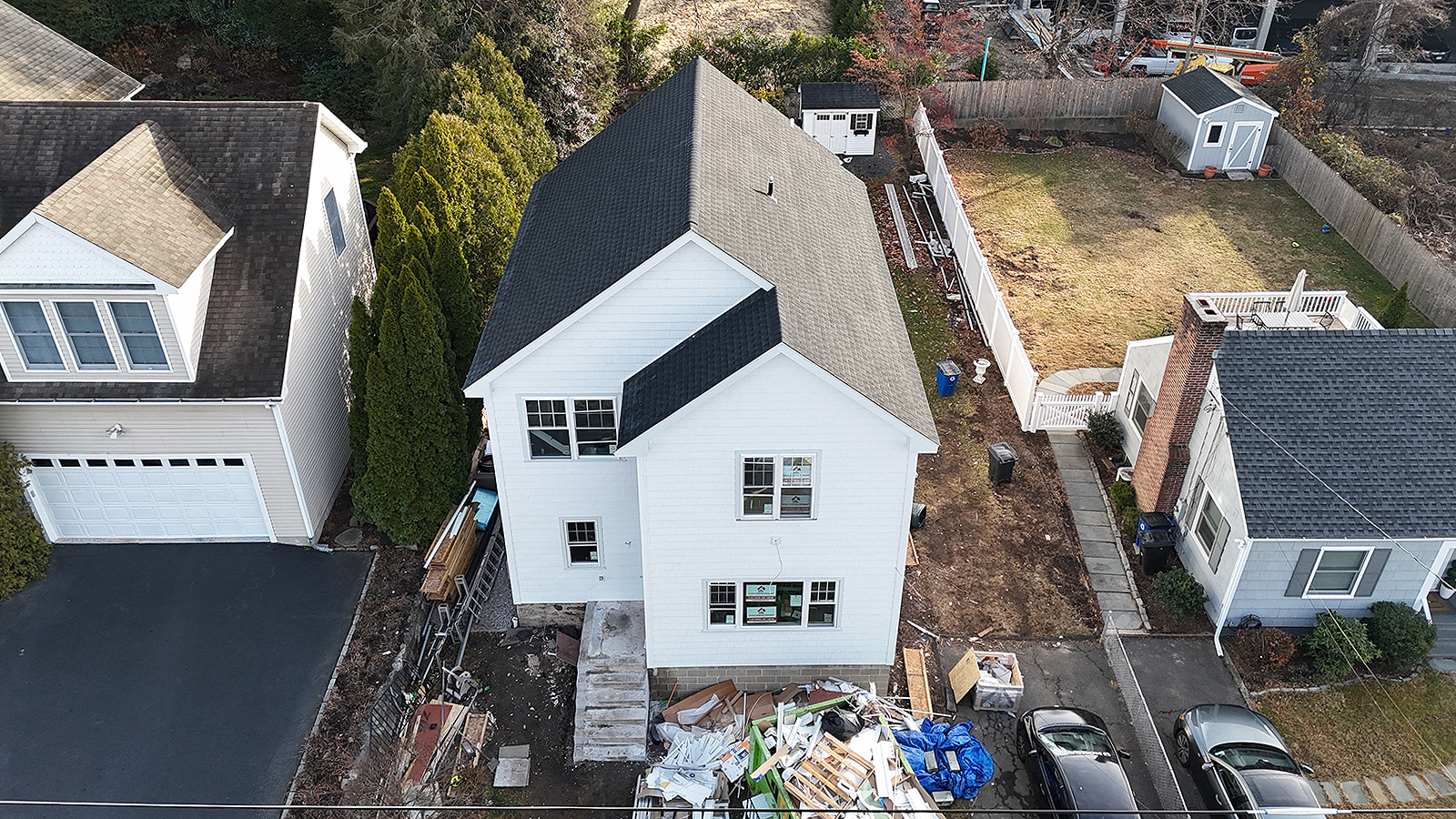 Home remodeling services in Connecticut. Aerial view of a white two‑story house under renovation, with construction debris in the front yard and neighboring homes on both sides.