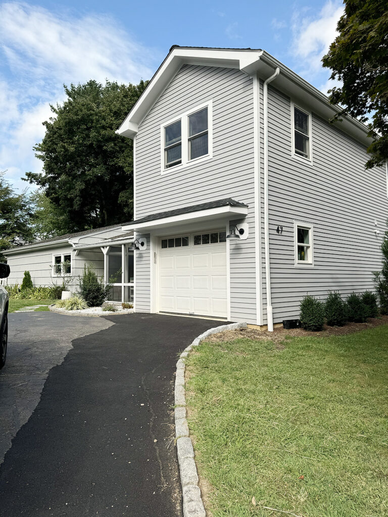 Home renovation and remodeling services in Connecticut. Two‑story gray house with white trim, an open garage, a paved driveway, and a fenced backyard.
