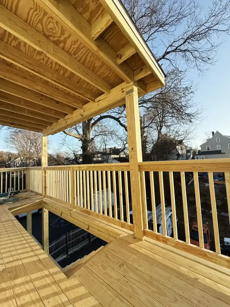 Home addition contractor in CT. Elevated wooden deck under construction with a roof, railings, and a view of the street below.